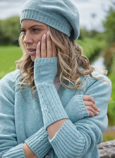 Woman wearing Fisherman wool-cashmere handwarmers in sea stone with classic Aran cable stitching, styled with matching knitwear.